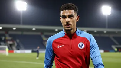 A determined 25-year-old Leyton Orient midfielder, athletic build, in a red and sky blue training top, intense eyes...