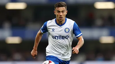 A 26-year-old, athletic, anonymous Leyton Orient striker, wearing a white jersey with blue sleeves and a blue collar, and...