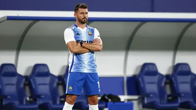 A tight action crop of a 30-year-old male football coach with a strong build, wearing a white jersey with a blue and...