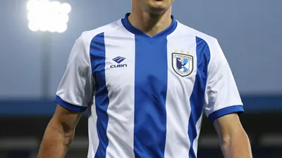 A head-and-shoulders photo of a young Leyton Orient player in action, wearing the team's blue and white kit, with a...