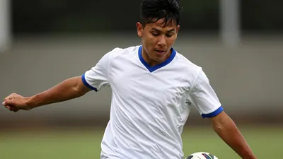 A close-up shot of a young, anonymous striker in a white jersey with blue sleeves and a blue collar, taken with a 50mm...
